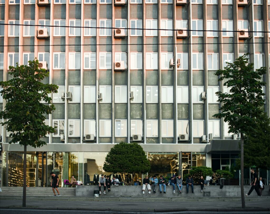 pexels-photo-8935087-8935087 Contemporary office facade with glass windows and people on urban street.